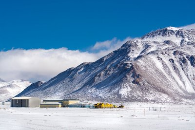 Mehrere flache Gebäude in einer verschneiten Landschaft; rechts von den Häusern befindet sich ein großer Berg.