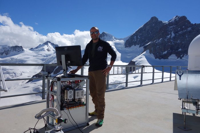 PSI-Forscher Federico Bianchi arbeitet in einer Berglandschaft unter freiem Himmel vor einem Monitor, der auf einem Massenspektrometer steht.