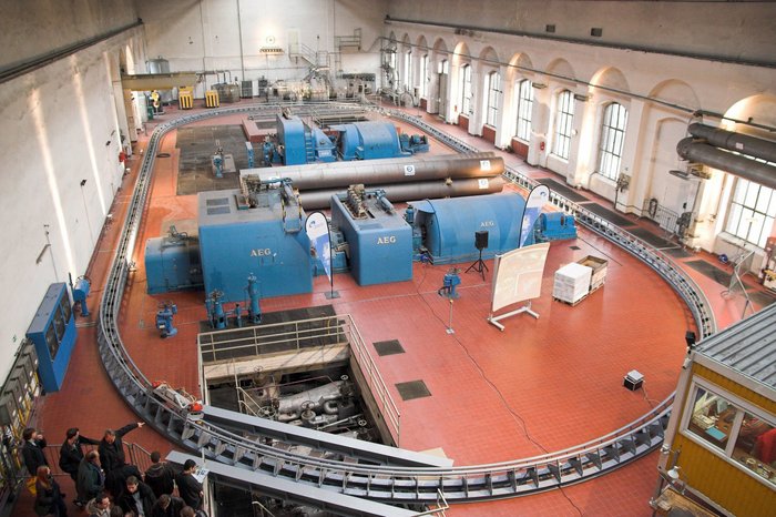 Modellstrecke für das CargoCap-System Foto: Halle, darin Gleisoval, in der Mitte elektrische Maschinen. Im linken unteren Eck eine Gruppe, die die Anlage besichtigt.