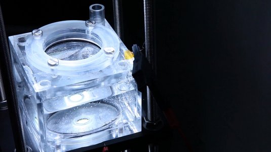 Foto eines transparenten Glaskastens mit Öffnung oben, der von hellem Licht angeleuchtet wird. Darin Wasser, in dem Bläschen aufsteigen.