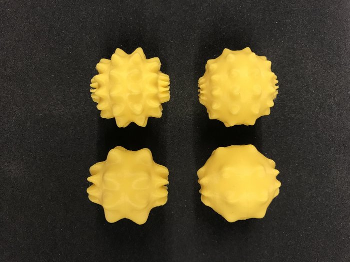 Vier gelbe Bälle mit verschiedenen Oberflächen vor grauem Hintergrund