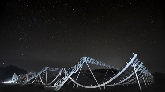 Mehrere große Metallbögen, über die Leitergänge verlaufen, unter einem Sternenhimmel