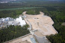 Luftbild einer großen gerodeten Fläche in einem Waldstück, links sind Gebäude des GSI Helmholtzzentrums zu sehen. Im hinteren Teil ist eine ringförmige Schneisesichtbar, wo später ein Beschleunigerring entstehen soll.