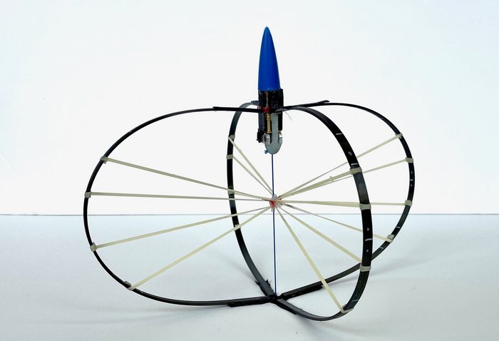 Zwei ineinander verschränkte Reifen, die mit mehreren Seilen miteinander verbunden sind, oben eine zapfenförmige Apparatur