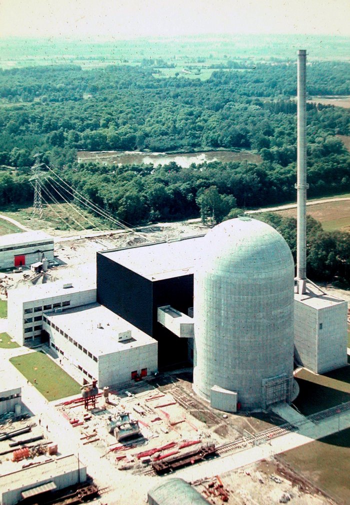 Baustelle eines Kernkraftwerks aus der Vogelperspektive. Ein zylindrischer, oben kuppelförmig abgeschlossener Betonbau, dahinter quaderförmige Hallen.