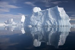 Ein spitzer weißer Eisberg von offensichtlich großen Ausmaßen schwimmt auf einem tiefdunkelblauen Wasser.