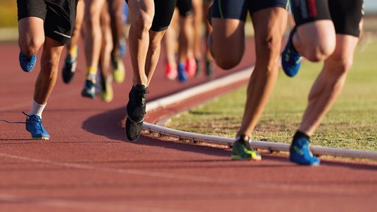 Leichtathleten laufen auf einer Tartanbahn. Es sind nur die Beine der Sportler zu sehen.