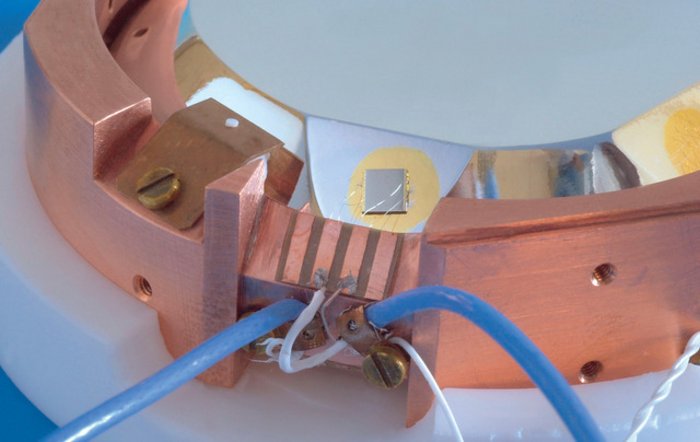 Detailansicht eines Germanium-Bolometers mit aufgeklebtem Wärmesensor Kristall, auf dem ein winziger Sensor klebt, in einer Kupfer-Halterung, an die Kabel angeschlossen sind.