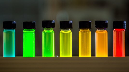 Auf dem Foto sind sieben kleine Glasfläschchen zu sehen, gefüllt mit farbigen Flüssigkeiten.