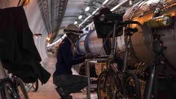 Eine Frau mit Schutzhelm hockt im Tunnel vor einem Laptop, der neben dem Beschleunigerrohr aufgebaut ist. Neben ihr sind Fahrräder abgestellt.