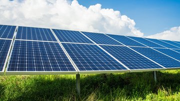 Das Foto zeigt eine Photovoltaikanlage auf einer grünen Wiese und vor einem blauem Himmel.