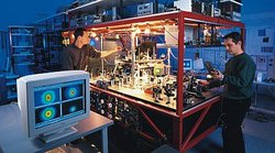 Zwei Männer arbeiten an einem hell erleuchteten Laser-Experiment. Monitor im Vordergrund.