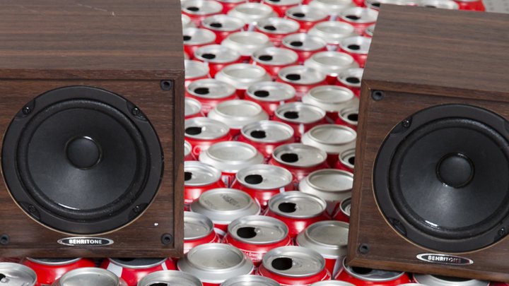 Viele Getränkedosen sind dicht nebeneinander angeordnet, darauf stehen zwei Lautsprecher und ein Mikrofon.