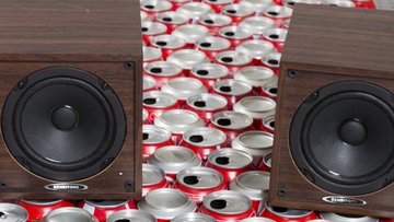 Viele Getränkedosen sind dicht nebeneinander angeordnet, darauf stehen zwei Lautsprecher und ein Mikrofon.