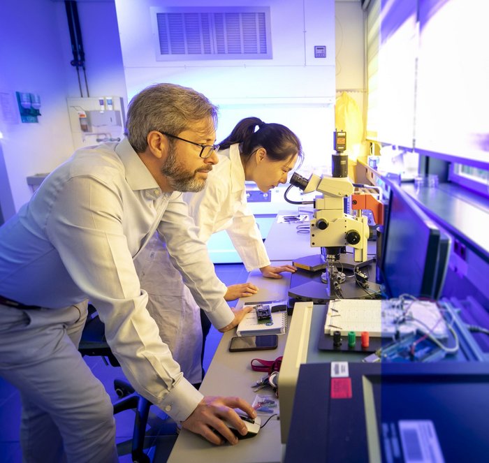 Im Labor Eine Wissenschaftlerin steht in einem Labor und schaut in ein Mikroskop. Ein zweiter Wissenschaftler steht daneben und bedient einen Computer.