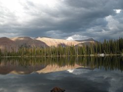 Landschaft mit einem See, indem sich Berge und Bäume spiegeln.