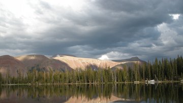 Landschaft mit einem See, indem sich Berge und Bäume spiegeln.