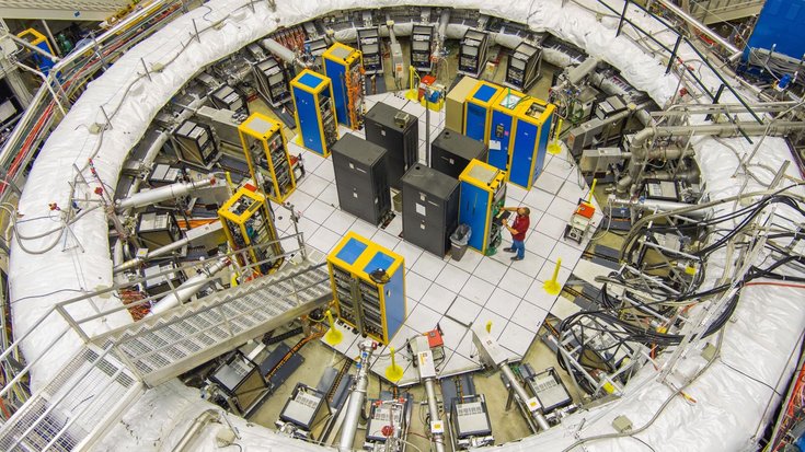 Der Muon g-2 Speicherring mit 14 Meter Durchmesser am Fermi National Accelerator Laboratory | Bildquelle: Ryan Postel/Fermilab Große kreisförmige Versuchsanordnung, in deren Mitte sehr viele Apparaturen und Computer stehen, die von Wissenschaftlern bedient werden