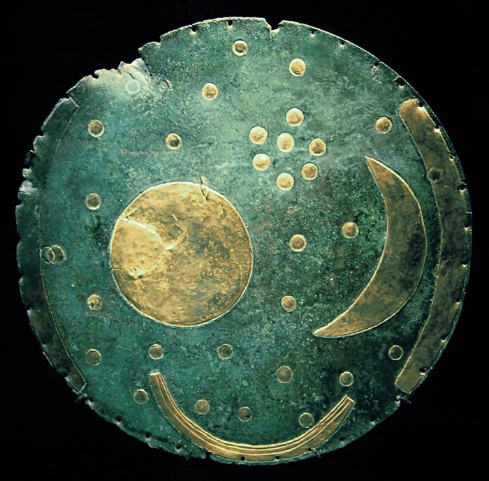 Die Himmelsscheibe von Nebra Eine dunkelgrüne, leicht verbeulte scheibe auf der in goldener Farbe ein Halbmond, ein großer Kreis und einige kleine Kreise aufgemalt sind.