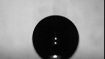 Ein dunkles Rundes Objekt befindet sich knapp oberhalb einer Platte