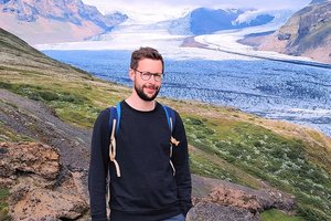 Porträt des Wissenschaftlers Fabian Zahnow vor einer gebirgigen Landschaft mit Gletscher.