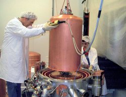 Zwei Personen in Schutzkleidung arbeiten daran, einen Kupferzylinder in eine komplexe Halterung zu montieren.
