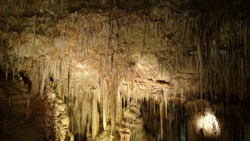 In einer dunklen Höhle werden durch eine Lichtquelle die nach unten hängenden Formationen von der Decke einer Tropfsteinhöhle gezeigt. 