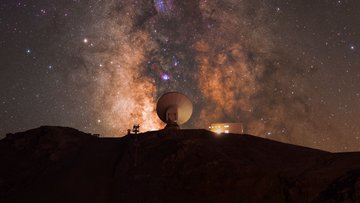 Parabolantenne bei Nacht, am Himmel ist geradezu leuchtend die Milchstraße zu sehen