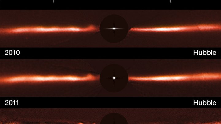 Die Staubscheibe ist als dünne Struktur rechts und links vom durch eine dunkle Scheibe abgedecktem Stern zu sehen und zeigt Verdichtungen an unterschiedlichen Stellen.