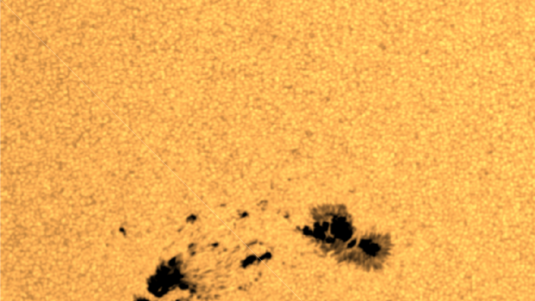 In der Nahaufnahme ist ein Sonnenfleck zu sehen, also eine dunklere Region auf der Sonnenoberfläche, die einige tausend Grad Celsius kühler ist als die umgebende Oberfläche. Rechts unten im Bild befindet sich die Erde maßstabsgetreu zum Größenvergle