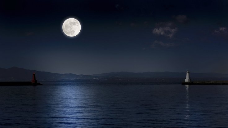 Bildquelle: kyoshino/iStock Foto einer Meeresbucht bei Nacht, links wirft der Vollmond weißes Licht auf die Wasseroberfläche, rechts steht ein heller Leuchtturm
