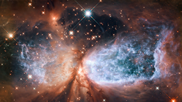 Eine Wolke aus rostrot leuchtendem Staub von dunklem Hintergrund mit einzelnen, funkelnden Sternen. Links und rechts vom Bildzentrum sind zwei runde Ausschnitte, in denen der Nebel blau leuchtet