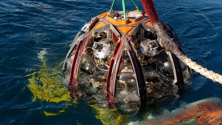 Ein Detektor des Neutrinoobservatoriums KM3NeT/ARCA | Bildquelle: Patrick Dumas/CNRS Ein runde Maschine, die an einem Haken hängt und gerade aus dem Meer gezogen wird