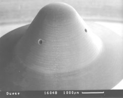 Mikroskopaufnahme eines hütchenförmigen Metallteils, das kleine Löcher an den Seiten aufweist, die als Einspritzdüsen dienen.