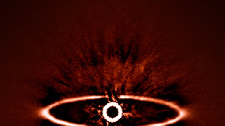 Ein abgedunkelter Stern mit Korona, um ihn herum ein flacher, ellipsenförmiger, heller Ring.