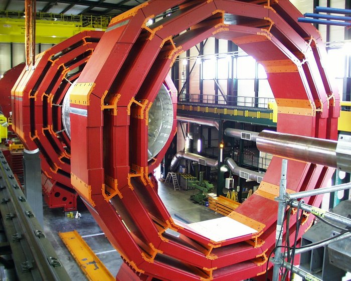Die Eisenstrukturen des Magneten für das CMS-Experiment Foto von mehreren riesigen, ringförmigen Konstruktionen aus Eisen, die hochkant in einer mehrstöckigen Montagehalle aufgebaut sind und den gesamten Raum vom Fußboden bis zur Hallendecke einnehmen.