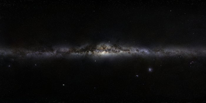 Auf dunklen Untergrund erstreckt sich das helle Band der Milchstraße, teilweise durch Dunkelwolken verdeckt.