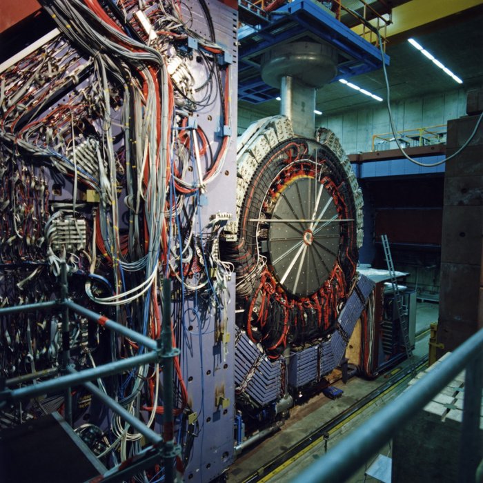 Der H1-Detektor in der HERA-Halle Nord Foto eines im Bau befindlichen, haushohen zylinderförmigen Nachweisgeräts für Elementarteilchen mit einer Vielzahl von technischen Komponenten und Tausenden von Kabeln.
