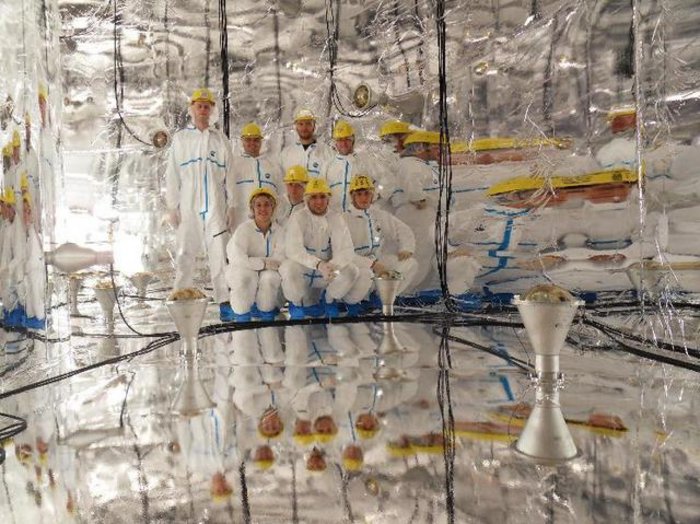 Forscher im GERDA-Detektor Menschen mit Helmen in einem Raum mit spiegelnden Wänden und spiegelndem Boden.
