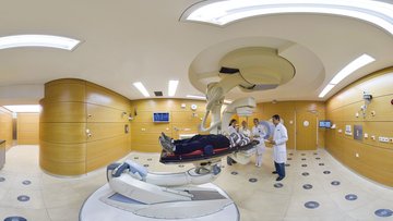Patient auf einer Liege im Behandlungsraum des Ionenstrahl-Therapiezentrums mit vier Ärzten