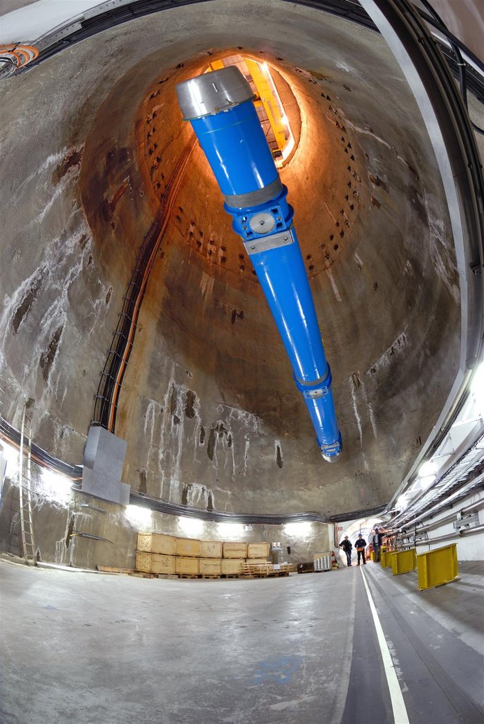 Der letzte Hauptdipolmagnet für den LHC wird herabgelassen Eine lange blaue Struktur wird in einen tiefen Schacht herabgelassen.