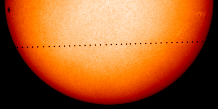 Ein Ausschnitt der Sonne ist zu sehen, über den sich eine Reihe kleiner schwarzer Scheibchen zieht.