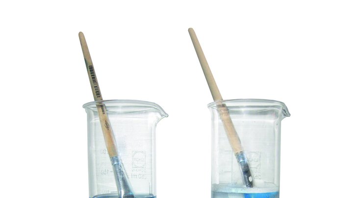 Zwei Pinsel mit blauer Farbe in Gläsern mit Pinselreinigern