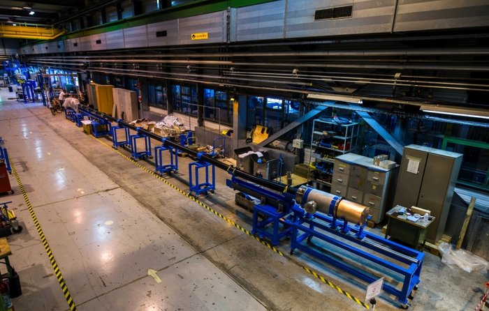 Prototyp eines supraleitenden Stromkabels Ein dunkles, mehrere Meter langes Rohr, das auf rollbaren Stützen in einer Versuchshalle aufgebaut ist. Am vorderen Ende ist es an eine Kühlstation angeschlossen.