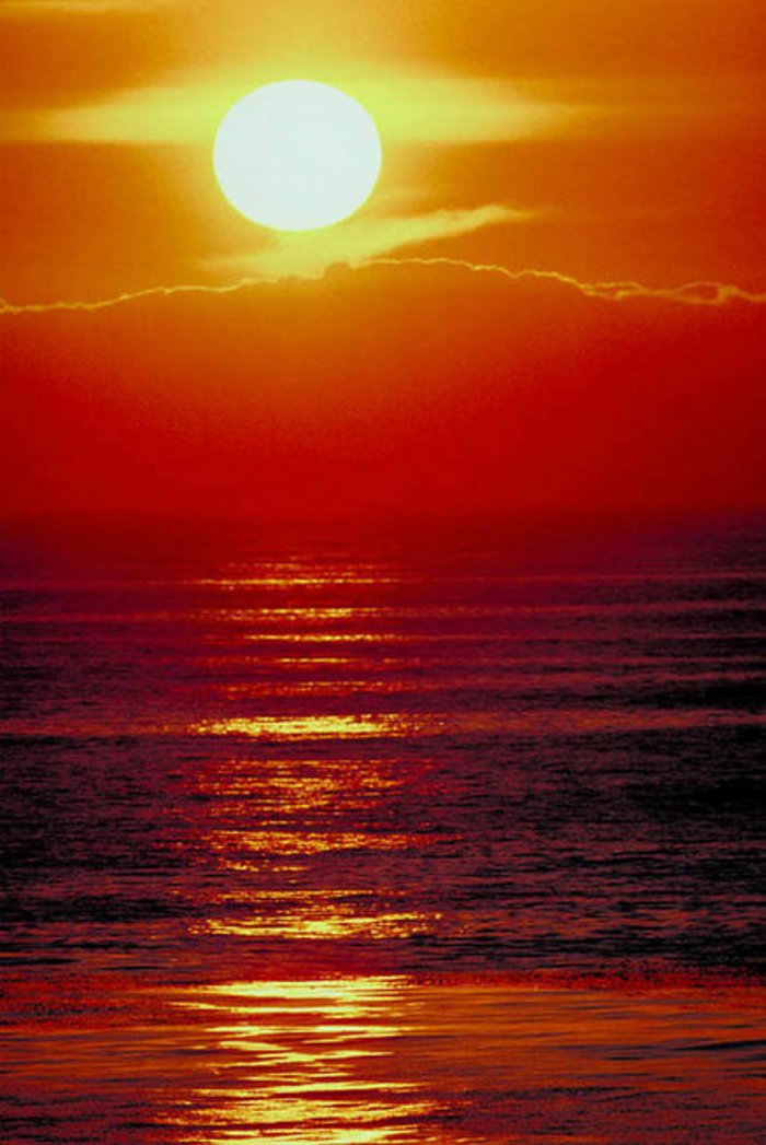 Sonnenuntergang über dem Meer. Die Sonne ist gelb eingefärbt, der Himmel um sie herum schimmert von orange um die Sonne herum bis dunkelrot direkt über dem Horizont