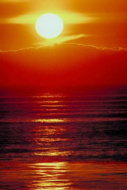 Sonnenuntergang über dem Meer. Die Sonne ist gelb eingefärbt, der Himmel um sie herum schimmert von orange um die Sonne herum bis dunkelrot direkt über dem Horizont 