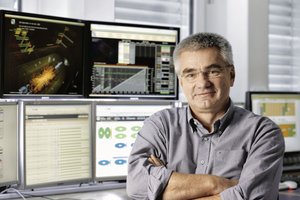 Porträt des Wissenschaftlers Joachim Mnich, im Hintergrund mehrere Monitore