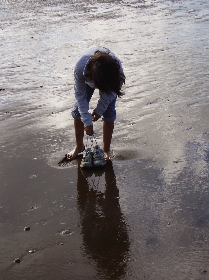 Fußabdrücke im Sand Dieses Foto zeigt eine Frau, die barfuss im feuchten Sand steht. Rund um ihre Füße wirkt der Sand heller und er reflektiert das Licht nicht so gut wie der Rest des Sandes. Der Sand ist also trockener.