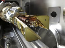 In einen mechanischen Arm ist ein weniger Zentimeter großer, zylinderförmiger Behälter eingespannt.