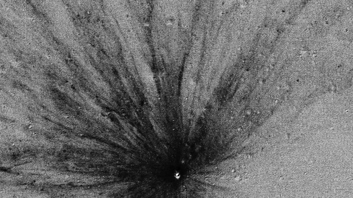 Kleiner heller Krater im Zentrum, von dem radial zahlreiche dunkle Strahlen ausgehen.